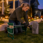 Woman using a green garden kneeler to install Halloween tombstone decorations in a lit front yard